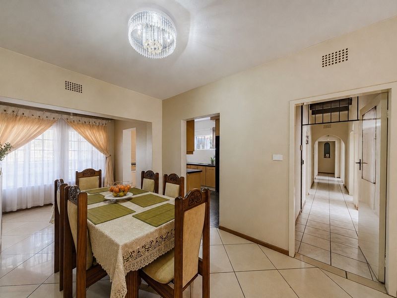A bright dining room featuring tiled flooring, a decorative crystal chandelier, and an open-plan layout connecting to the kitchen and hallway.