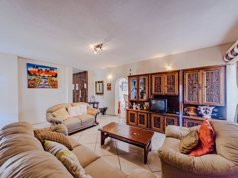 Spacious living room featuring tiled flooring, an arched entryway, and an exposed brick accent wall, offering a comfortable and traditional living space.