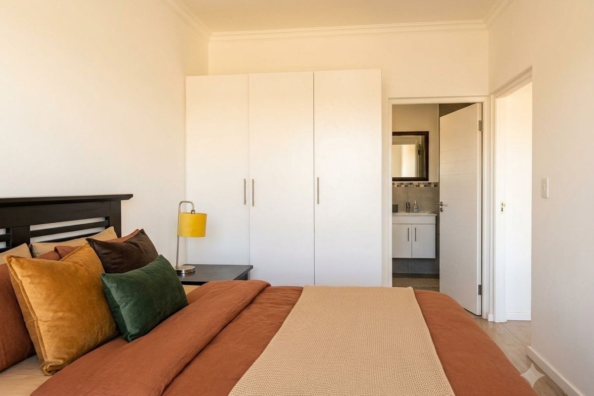A well-maintained bedroom featuring built-in cupboards, laminate flooring, and direct access to an en-suite bathroom.