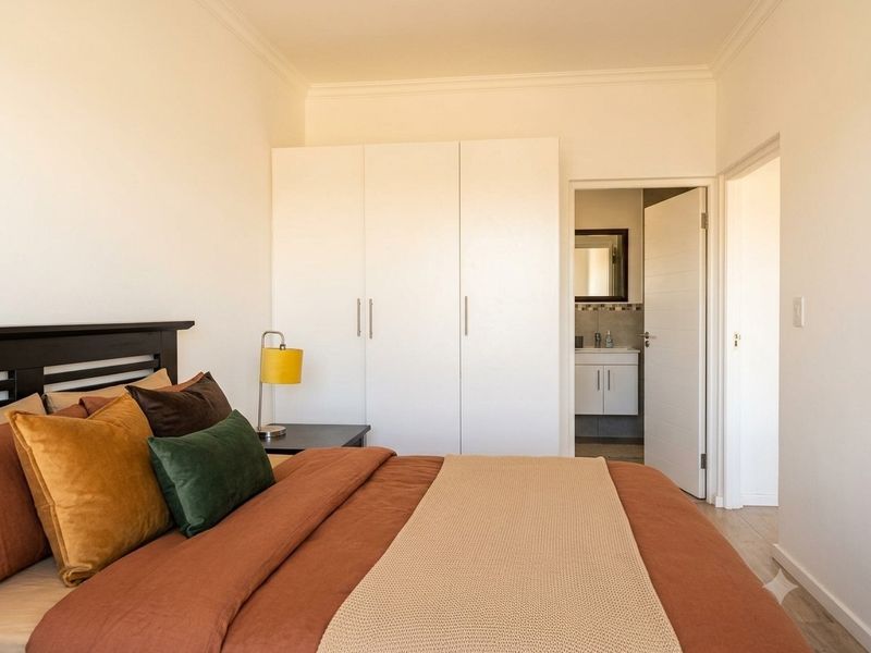 A well-maintained bedroom featuring built-in cupboards, laminate flooring, and direct access to an en-suite bathroom.