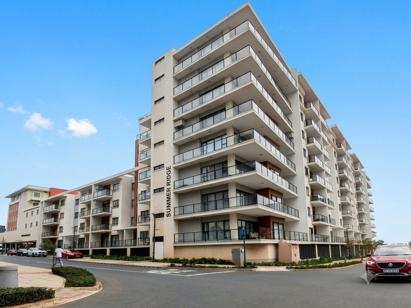 Exterior view of Summer Ridge apartment complex featuring modern multi-story architecture with glass-fronted balconies and paved street access.