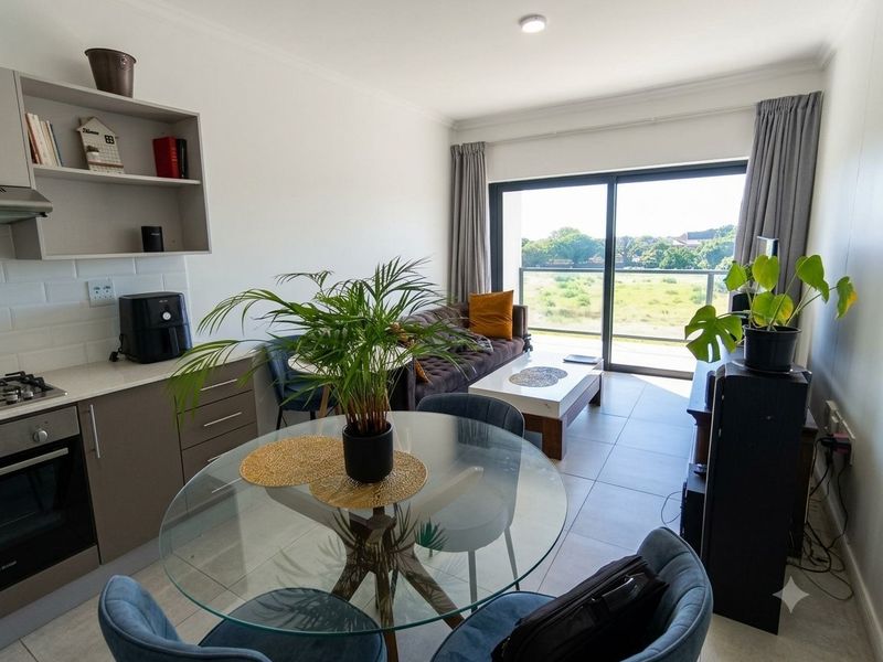 Modern open-plan living area featuring a compact kitchen with built-in appliances, tiled floors, and large sliding doors leading to a balcony with scenic views.
