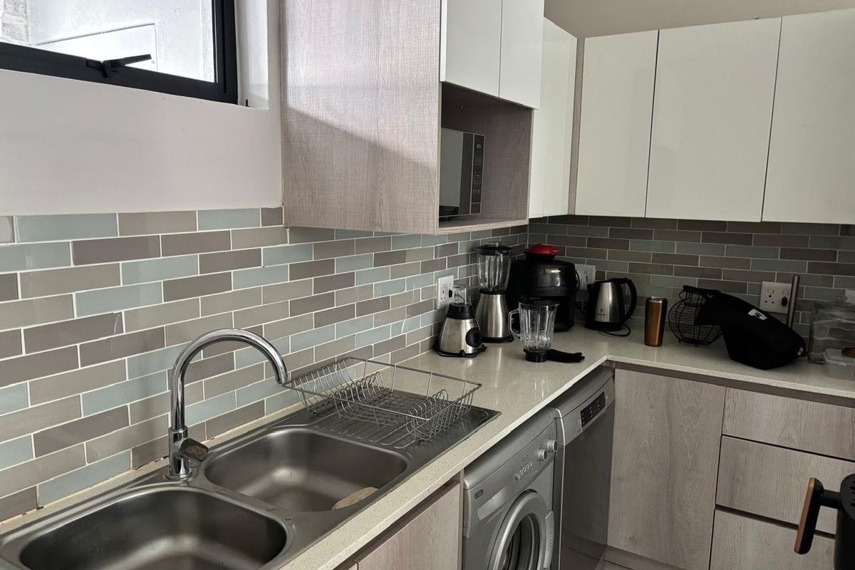 Modern kitchen featuring light wood-grain cabinetry, stone countertops, a double stainless steel sink, and a stylish subway tile backsplash.