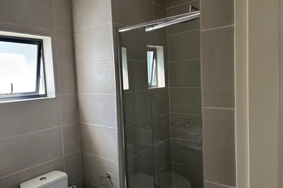 A modern bathroom featuring neutral wall tiles, a glass-enclosed shower, and a standard toilet.