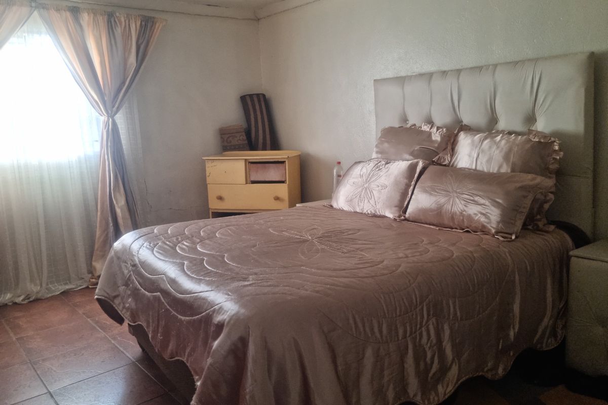 A bedroom featuring tiled flooring and a window with curtains. The room shows signs of wear on the walls and ceiling.