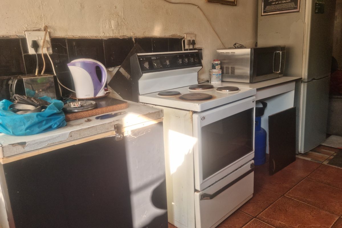 A dated kitchen area featuring a freestanding electric stove, tiled splashback, and terracotta floor tiles, requiring significant renovation and cosmetic updates.