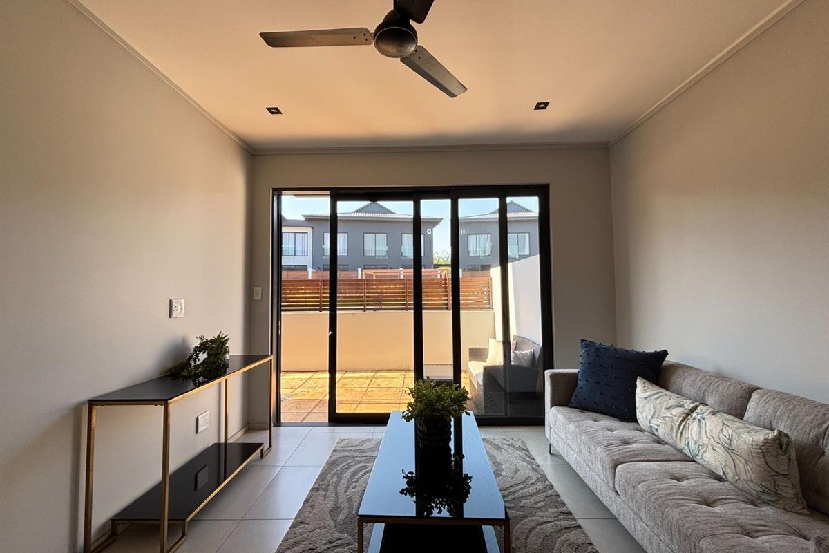 A bright living room featuring tiled flooring, a ceiling fan, and large sliding glass doors that open onto a private patio area.
