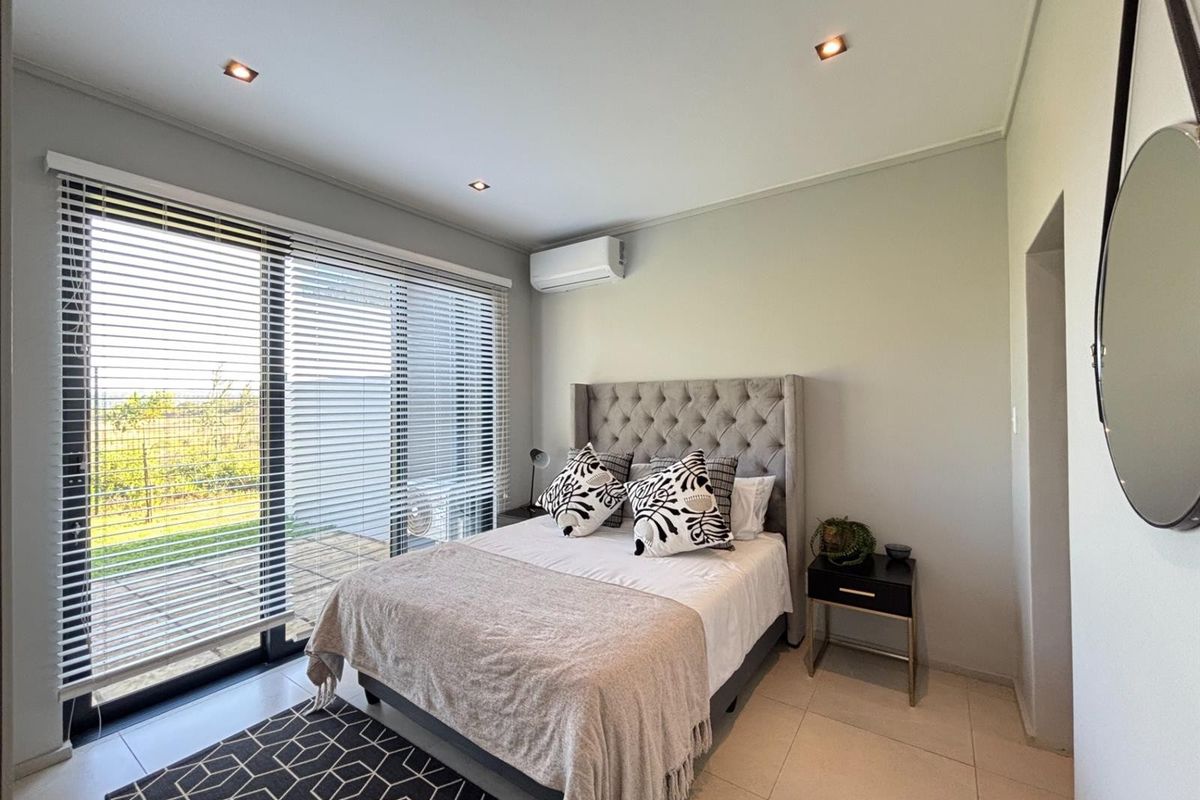 A well-maintained bedroom featuring tiled flooring, recessed ceiling lighting, a wall-mounted air conditioning unit, and large sliding glass doors leading to an outdoor area.