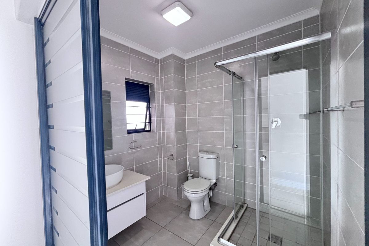 Modern bathroom featuring neutral floor-to-ceiling tiling, a glass-enclosed shower, a contemporary vanity with a basin, and a standard toilet.