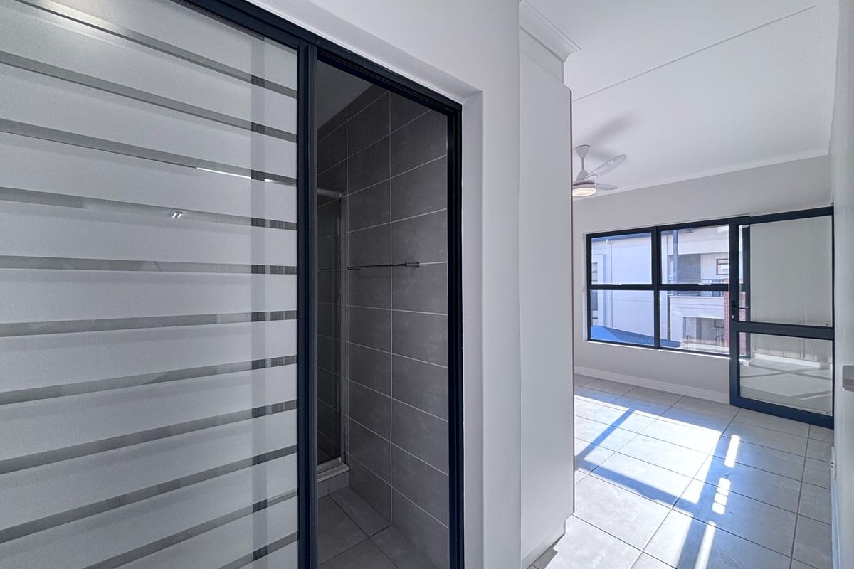 A bright, modern bedroom featuring tiled flooring, a ceiling fan, and an en-suite bathroom with a glass-panelled door and tiled shower enclosure.
