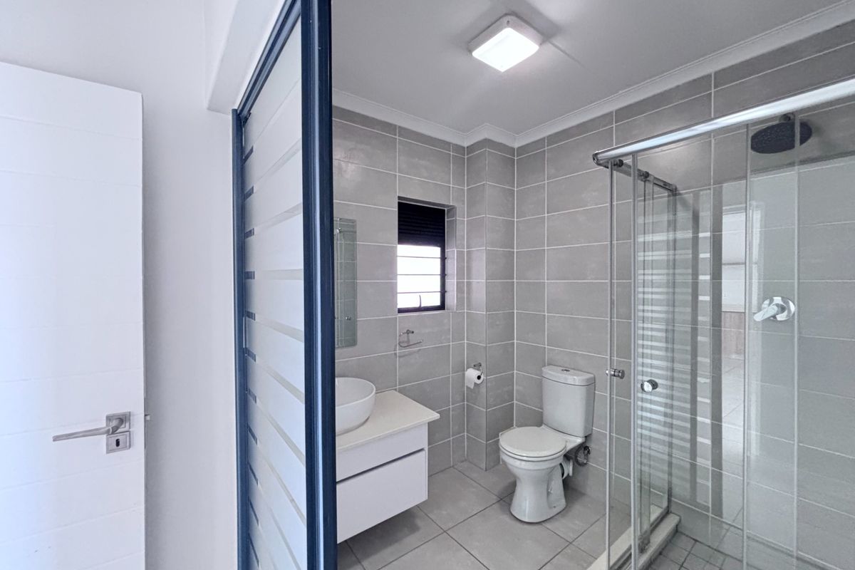 Modern bathroom featuring grey floor-to-ceiling wall tiles, a glass-enclosed shower, a white vanity with a vessel sink, and a toilet.