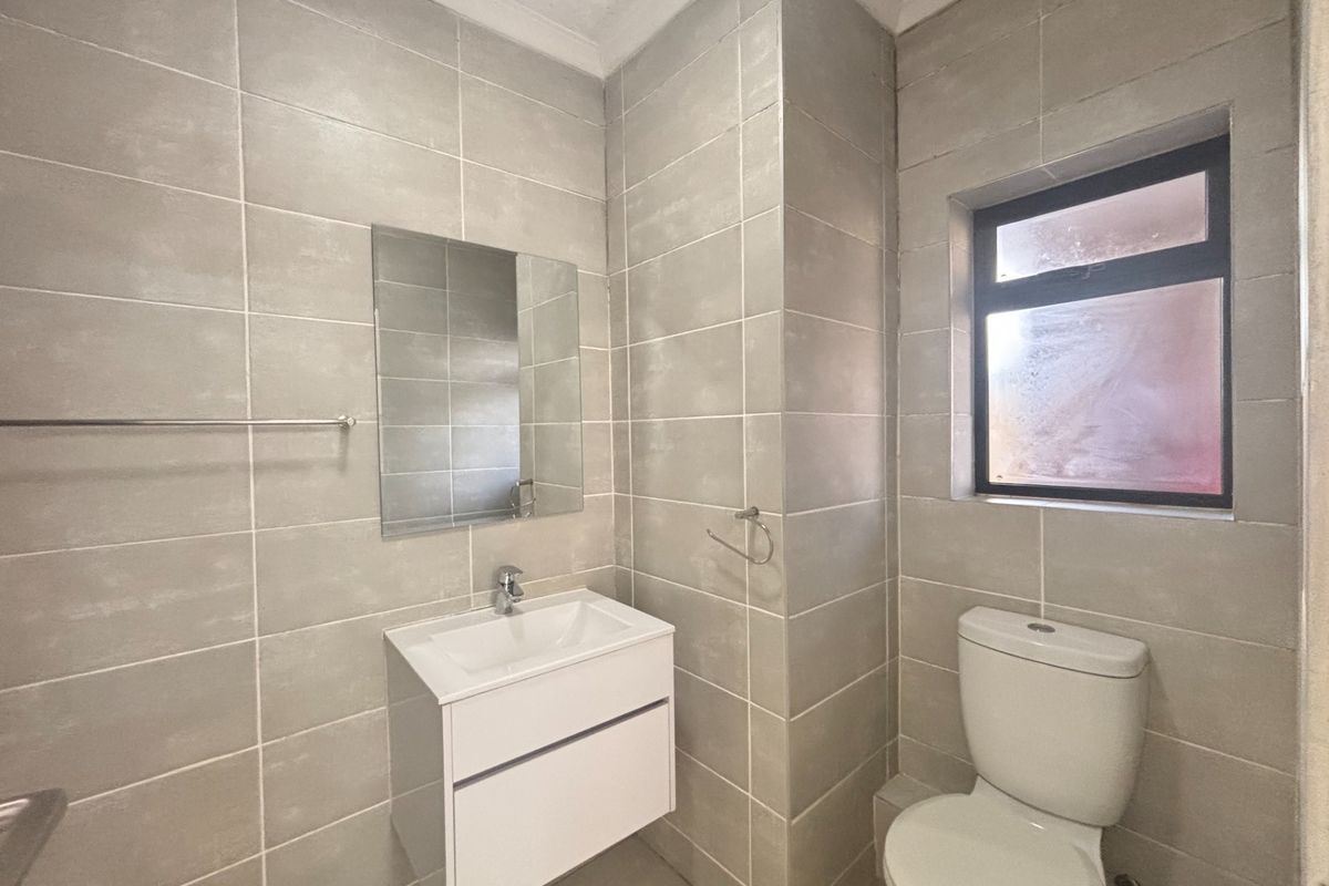 A modern, tiled bathroom featuring a wall-mounted vanity with a basin, a mirror, and a standard toilet.