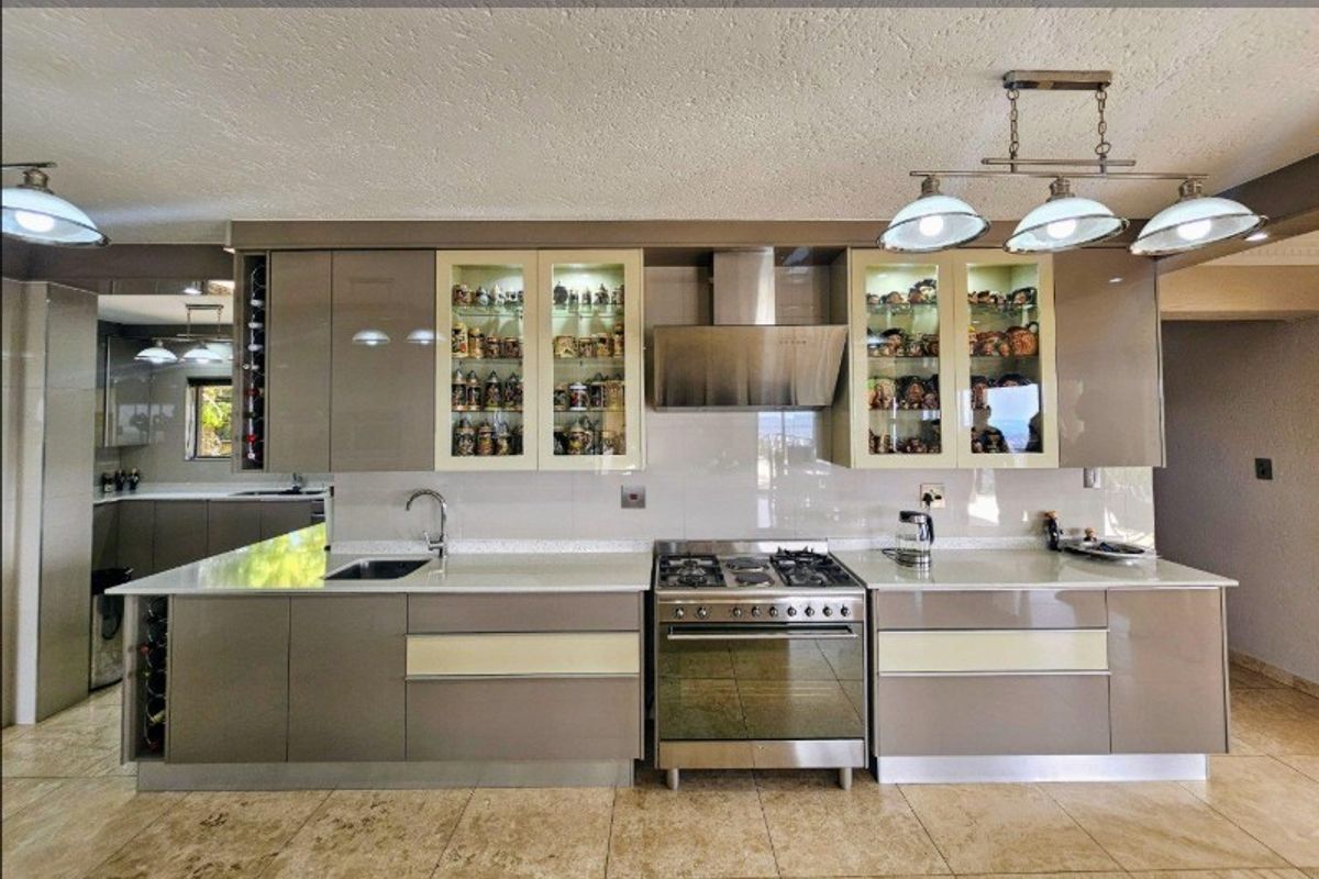 Modern kitchen featuring high-gloss cabinetry, stone countertops, a stainless steel gas range with extractor hood, and integrated glass-front display cabinets.