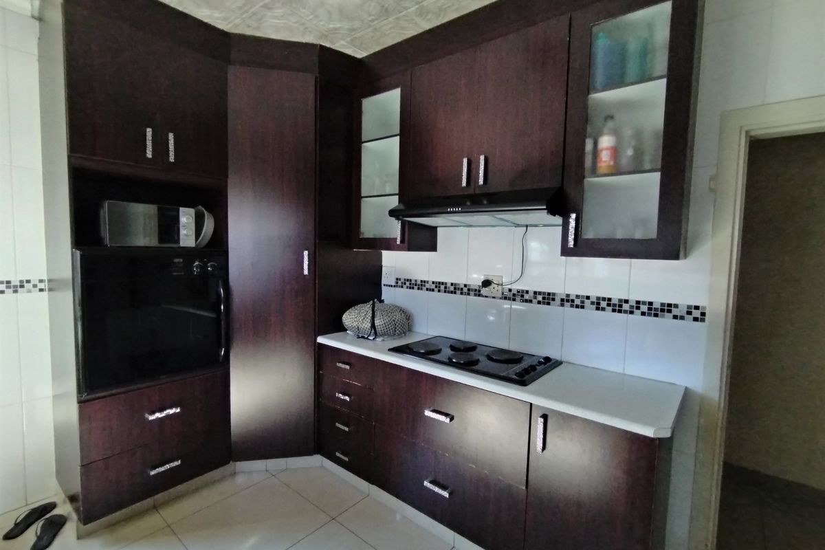 A functional kitchen featuring dark wood cabinetry, built-in oven, integrated hob, extractor fan, and tiled splashback with decorative mosaic accents.