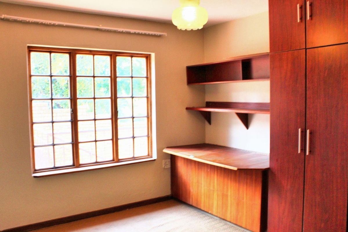 A bedroom featuring built-in wooden cabinetry, a desk, shelving, and a large window with wooden frames, providing a functional space with neutral finishes.