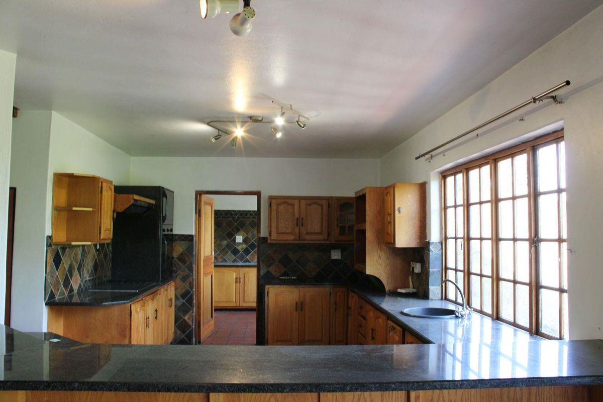 A functional kitchen featuring wooden cabinetry, granite countertops, a double sink, and a tiled backsplash, illuminated by modern track lighting.