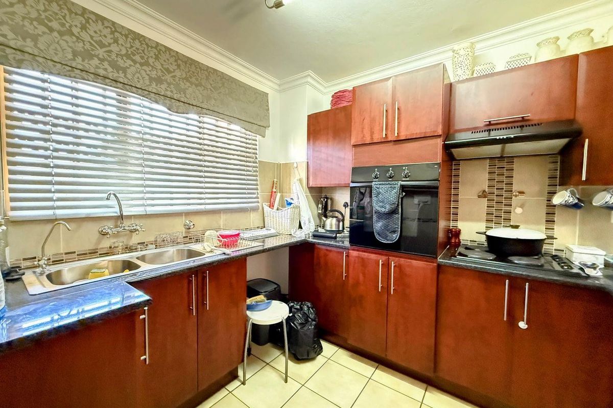 A functional kitchen featuring dark wood cabinetry, granite countertops, a built-in oven, hob with extractor fan, and a double basin sink.