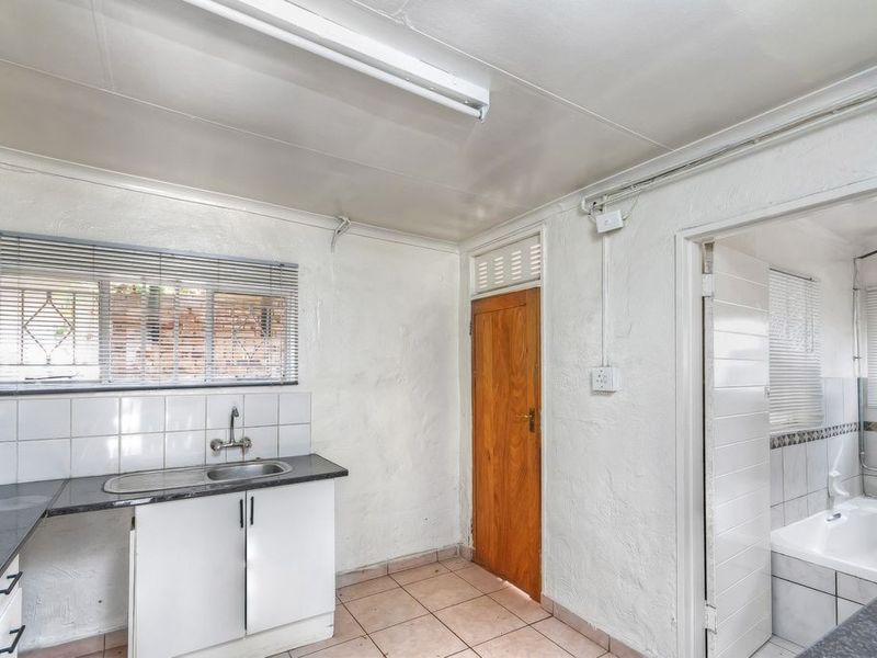 A functional kitchen area featuring a stainless steel sink, tiled splashback, and direct access to an adjacent bathroom.