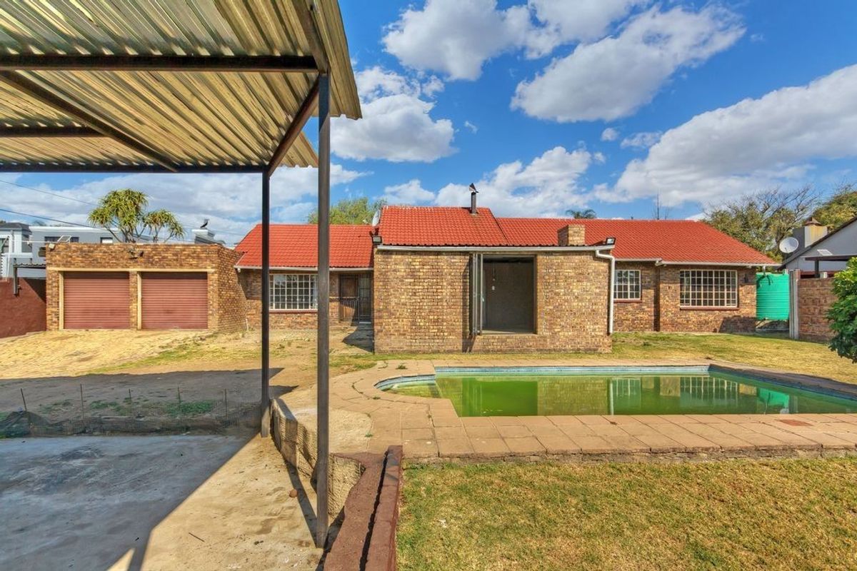 Rear view of a brick house featuring a swimming pool, covered patio area, and a detached double garage.