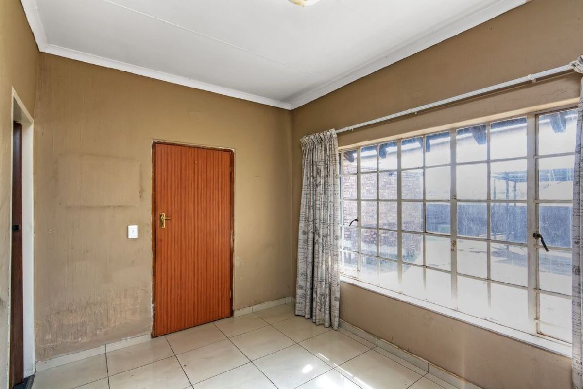An empty bedroom featuring tiled flooring, a large steel-framed window, and neutral wall finishes, offering a blank canvas for renovation or interior design updates.