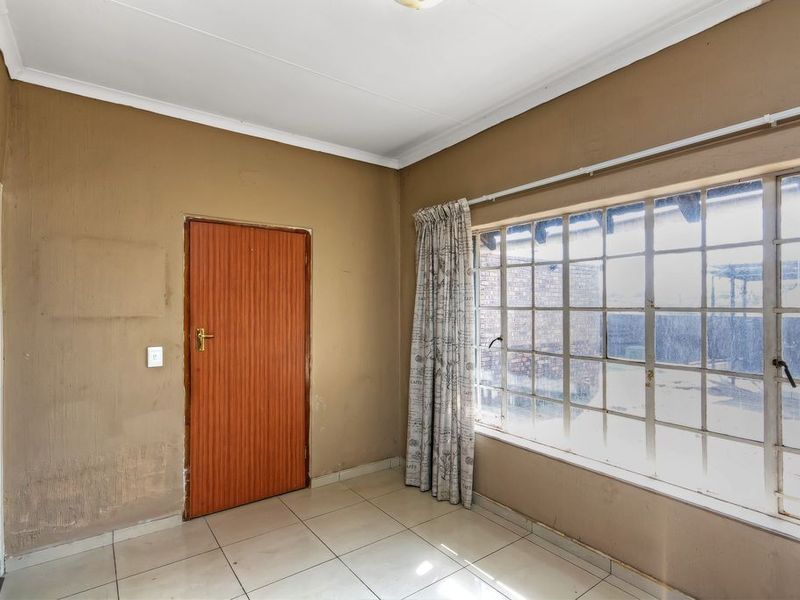 An empty bedroom featuring tiled flooring, a large steel-framed window, and neutral wall finishes, offering a blank canvas for renovation or interior design updates.