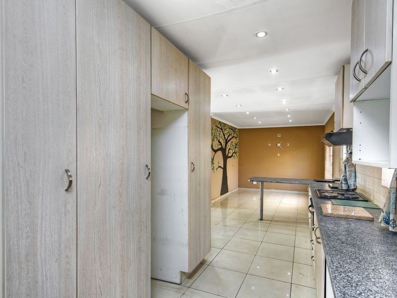 A functional kitchen featuring light wood-look cabinetry, granite countertops, a built-in hob with extractor fan, and tiled flooring throughout.