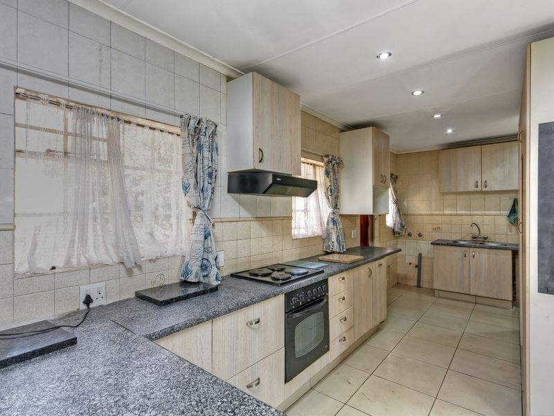 Functional kitchen featuring light wood-finish cabinetry, granite countertops, built-in oven with hob, and tiled flooring throughout.