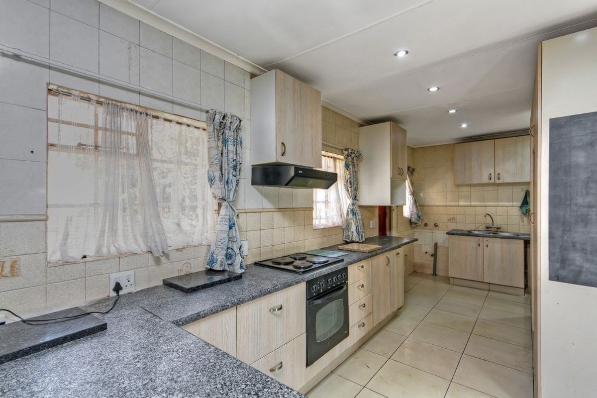 Functional kitchen featuring light wood-finish cabinetry, granite countertops, built-in oven with hob, and tiled flooring throughout.