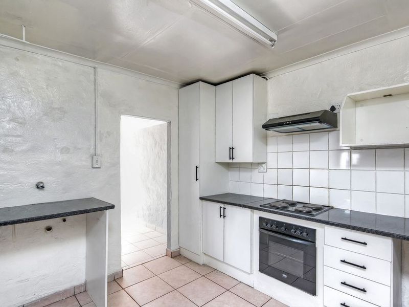 A compact, functional kitchen featuring white cabinetry, dark countertops, built-in oven and hob, and tiled finishes, ready for a modern update.