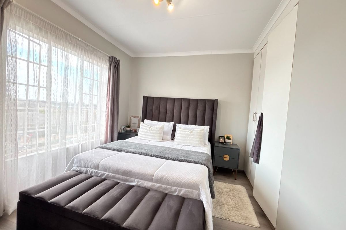 A well-maintained bedroom featuring built-in wardrobes, neutral wall finishes, and large windows that provide ample natural light.