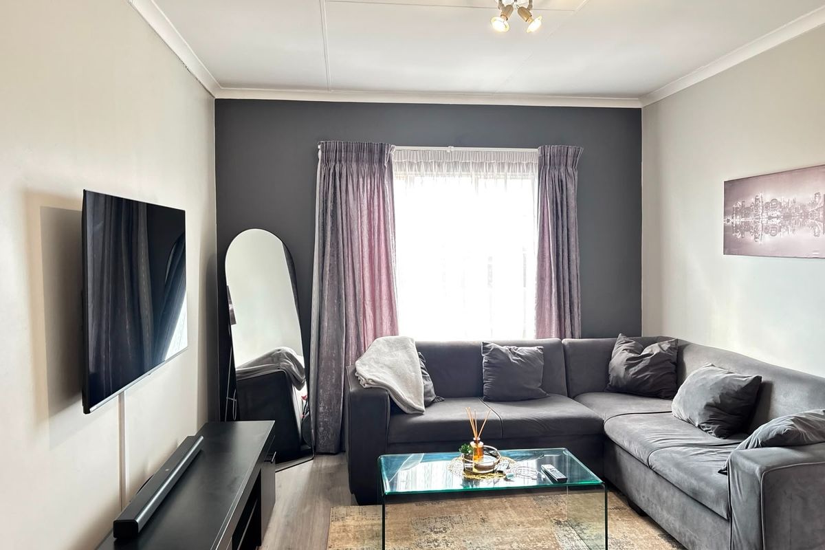 A comfortable living room featuring a dark accent wall, laminate flooring, and a large window with curtains, providing a cozy and functional space.