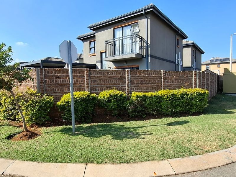 A view of the property exterior from the street, featuring a brick boundary wall, landscaped garden, and an upper-level balcony with metal railing.