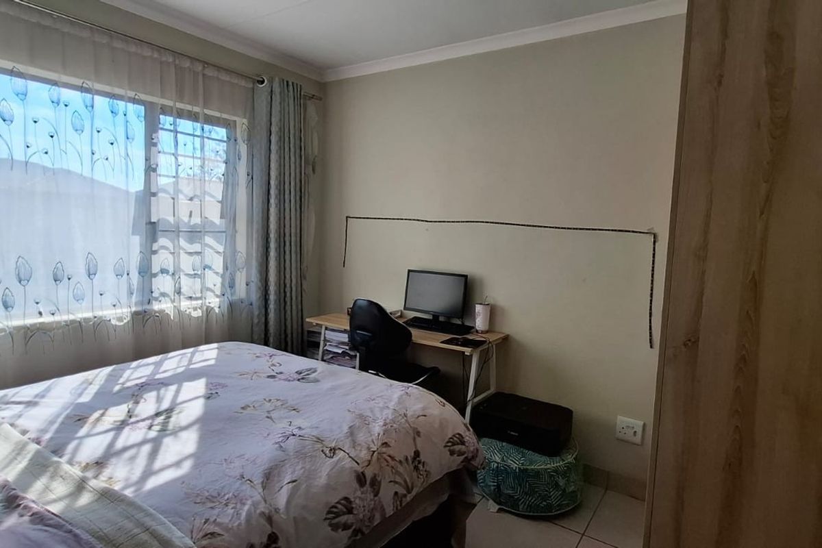 A functional bedroom featuring tiled flooring, a built-in cupboard, and a window with security bars, providing natural light and essential storage space.