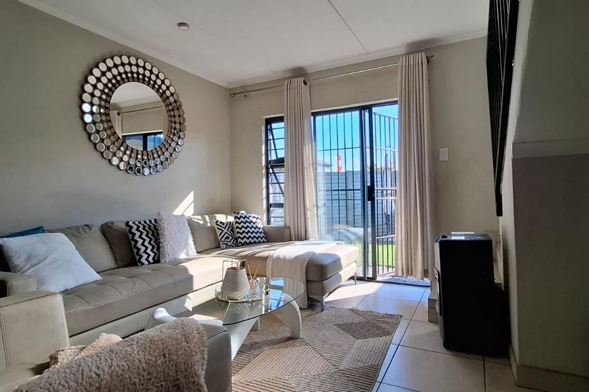 A bright living room featuring tiled flooring and a sliding glass door with a security gate, providing direct access to the outdoor area.