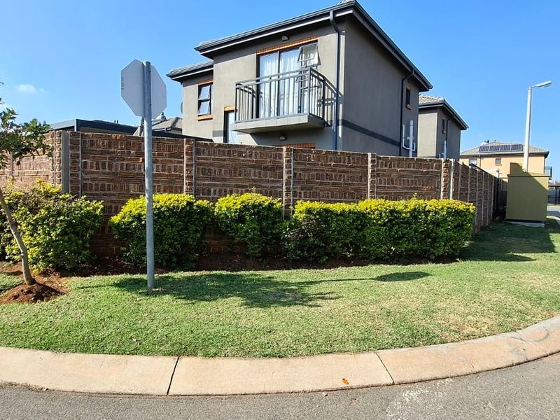 A street-level view of a modern residential property featuring a brick boundary wall, landscaped garden, and a balcony on the upper level.