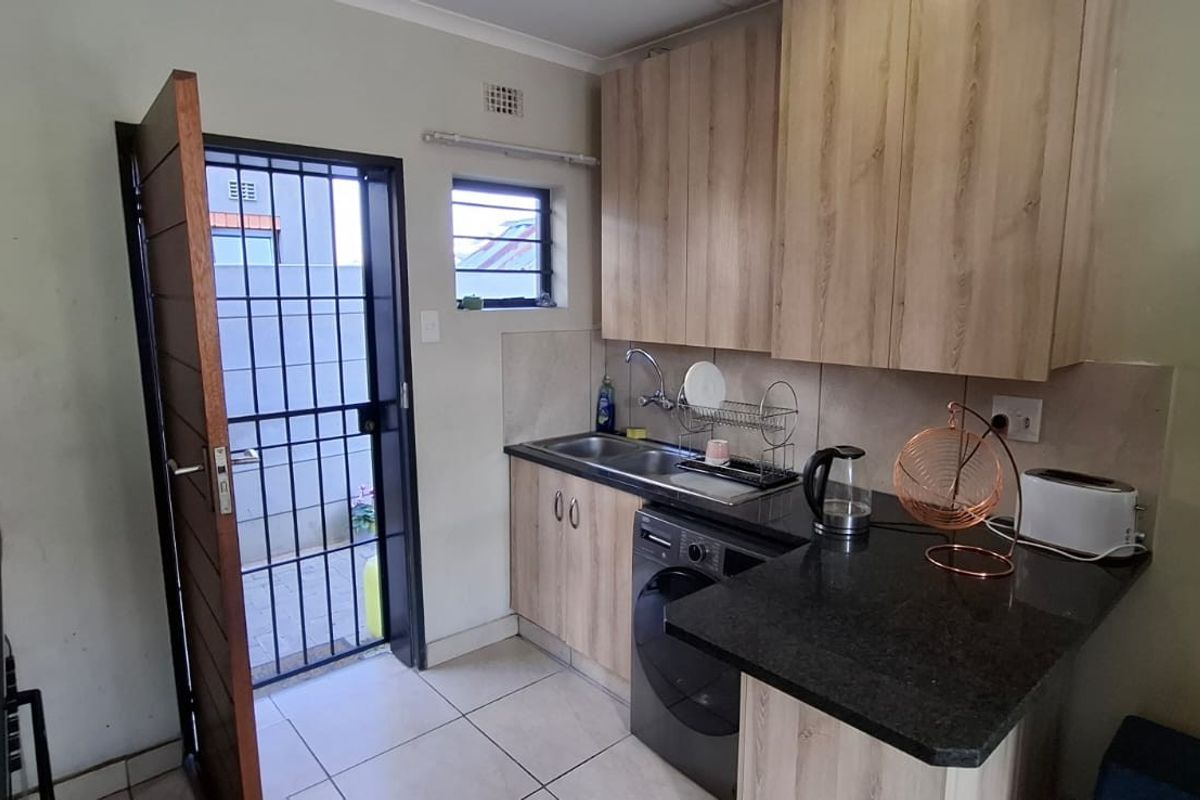 Compact kitchen featuring wood-look cabinetry, granite countertops, stainless steel sink, and direct access to an exterior area via a security gate.
