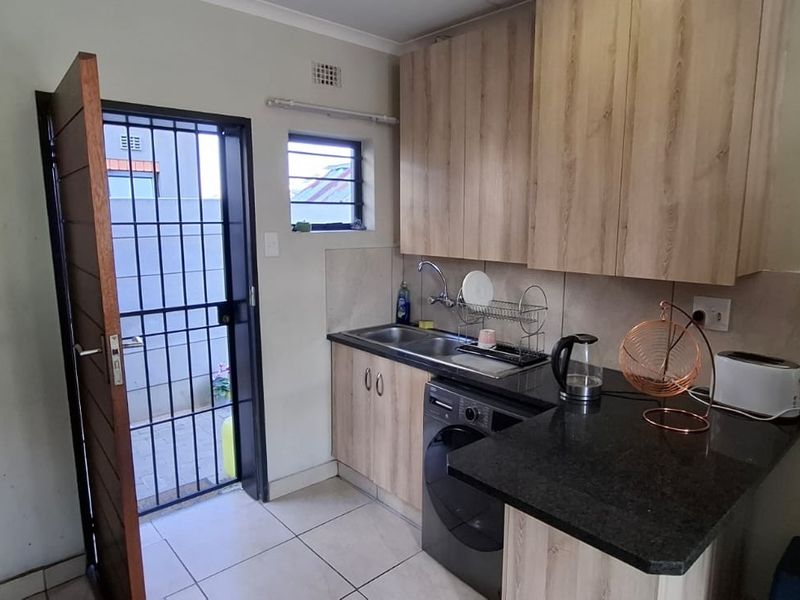 Compact kitchen featuring wood-look cabinetry, granite countertops, stainless steel sink, and direct access to an exterior area via a security gate.