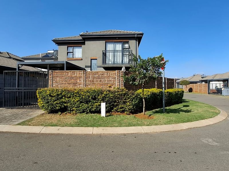 A view of the front elevation of a two-story residential house featuring a brick boundary wall, paved driveway, and a balcony.