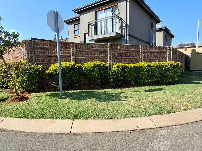 Street view showing the property's exterior brick boundary wall, landscaped verge, and a view of the upper-level balcony.