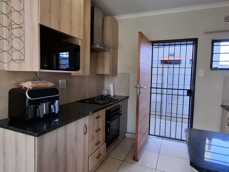Modern kitchen featuring light wood cabinetry, granite countertops, built-in oven and hob, and direct access to the exterior via a secure door.