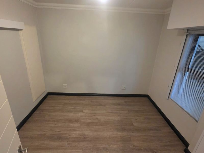 A clean, empty bedroom featuring modern laminate flooring, neutral walls, and a built-in cupboard, offering a versatile space ready for personalization.