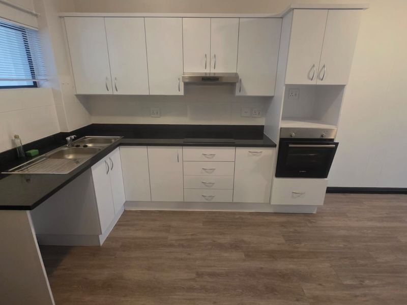 A clean, modern kitchen featuring white cabinetry, dark laminate countertops, built-in oven, extractor fan, and durable wood-look laminate flooring.