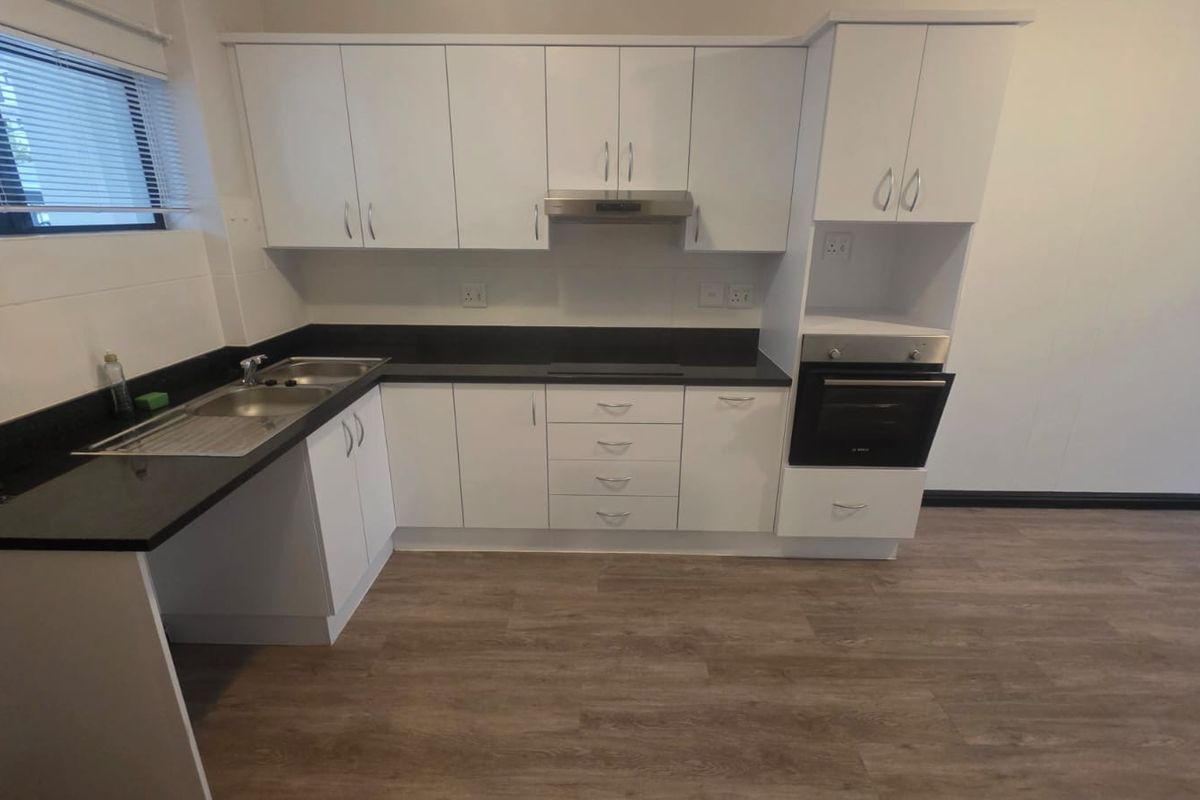 A clean, modern kitchen featuring white cabinetry, dark laminate countertops, built-in oven, extractor fan, and durable wood-look laminate flooring.