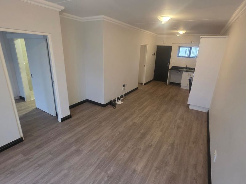 An open-plan living and kitchen area featuring modern laminate flooring, neutral walls, and functional built-in cabinetry, offering a clean and versatile space.