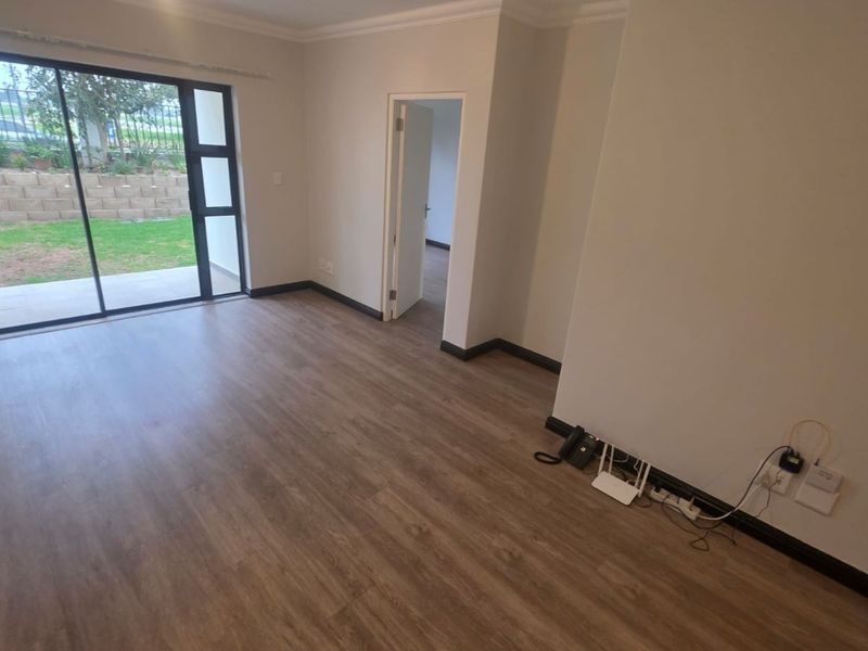 A bright, empty living room featuring modern laminate flooring, neutral walls, and a large sliding glass door providing access to the garden.