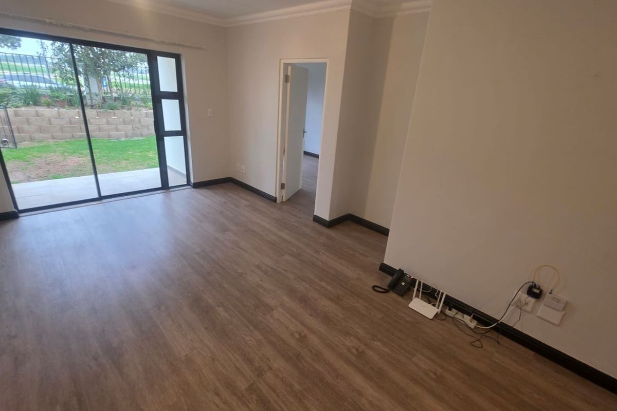 A bright, empty living room featuring modern laminate flooring, neutral walls, and a large sliding glass door providing access to the garden.