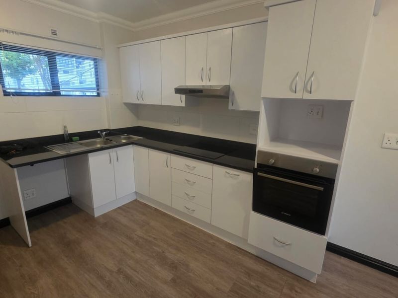 A clean, modern kitchen featuring white cabinetry, dark countertops, built-in oven, extractor fan, and durable vinyl flooring.