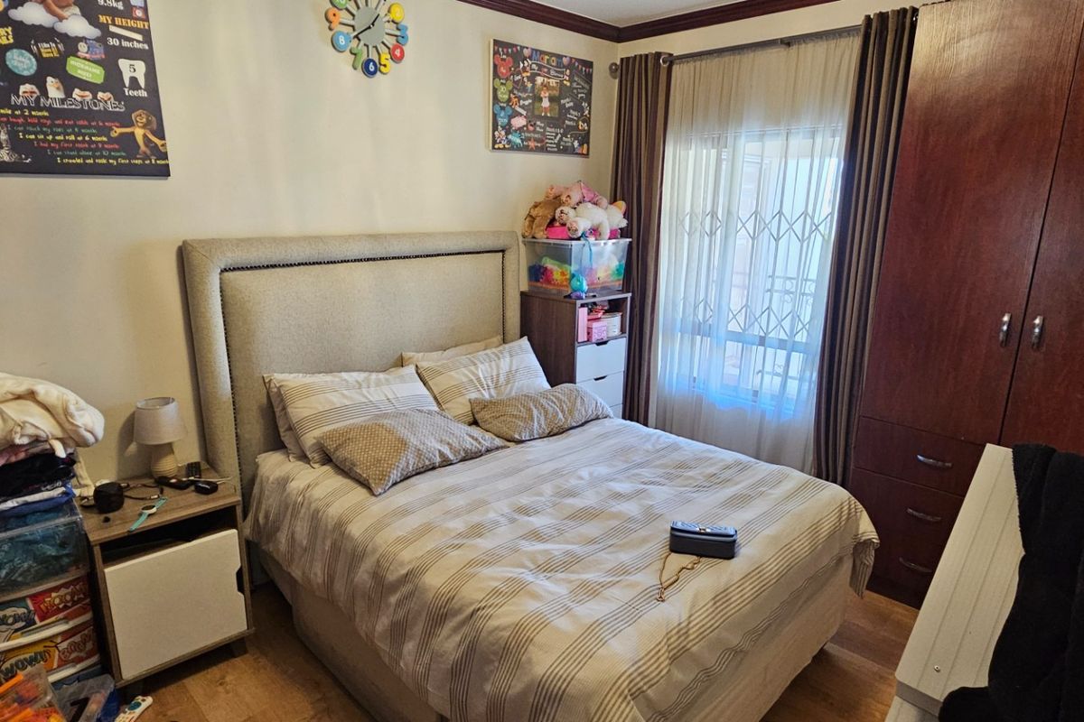 A bedroom featuring built-in wooden cabinetry, laminate flooring, and a window fitted with security bars and curtains.