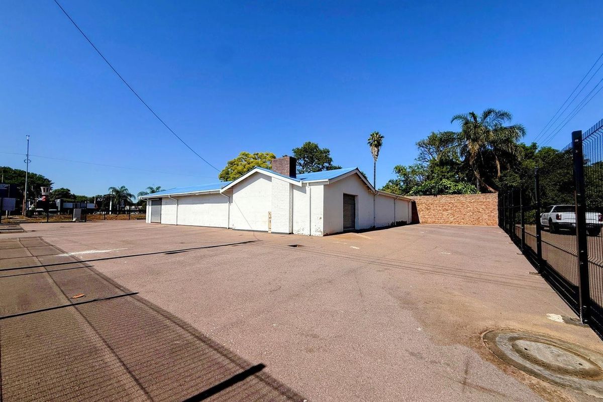 Rear exterior view of the property featuring a large asphalt parking area, brick boundary wall, and metal security fencing.