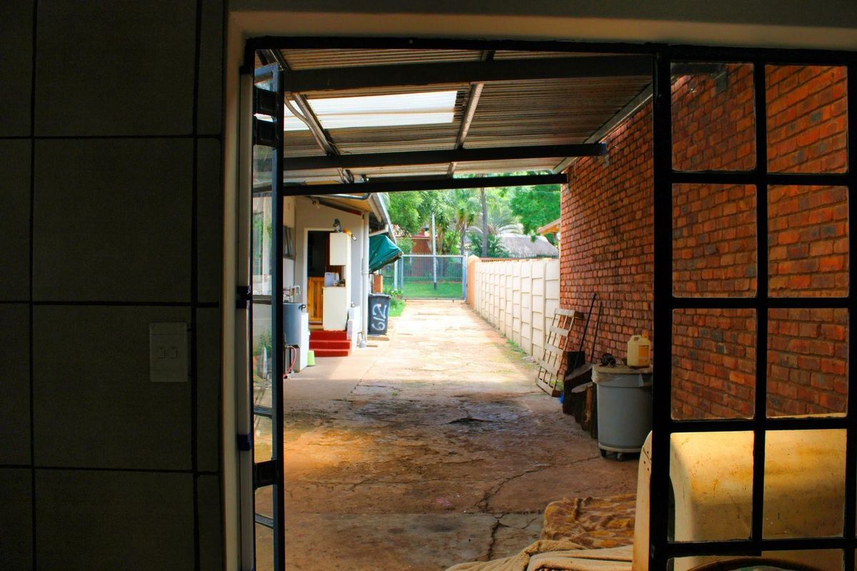 A view looking out from an interior space onto a rear driveway area featuring exposed brick walls, a corrugated roof, and a concrete boundary wall.